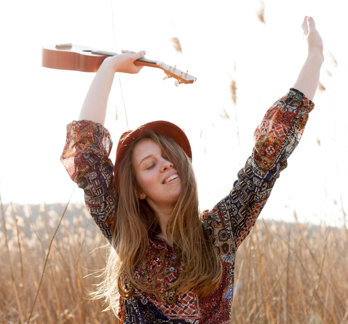 Frau mit Ukulele in der Hand tanz im Kornfeld